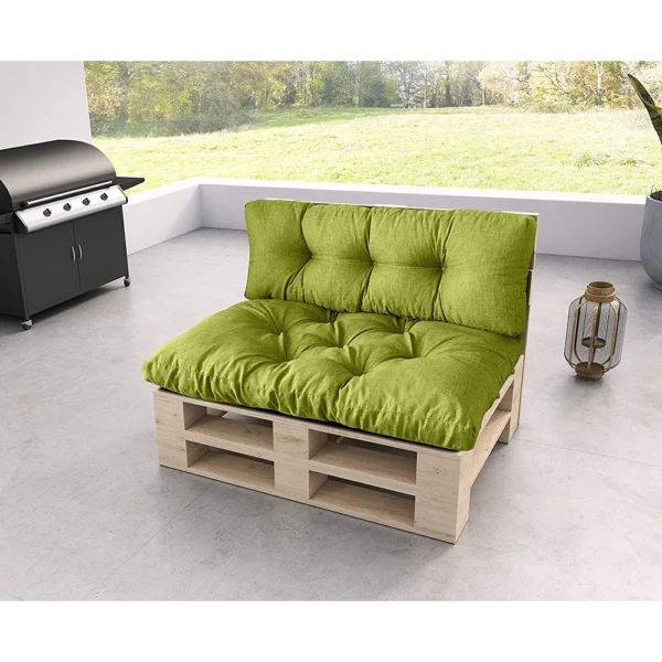 Zielona, wyściełana sofa z palet stoi na szarym patio w pobliżu czarnego grilla, z dekoracyjną latarnią obok i trawiastym podwórkiem widocznym przez szklane ściany w tle.